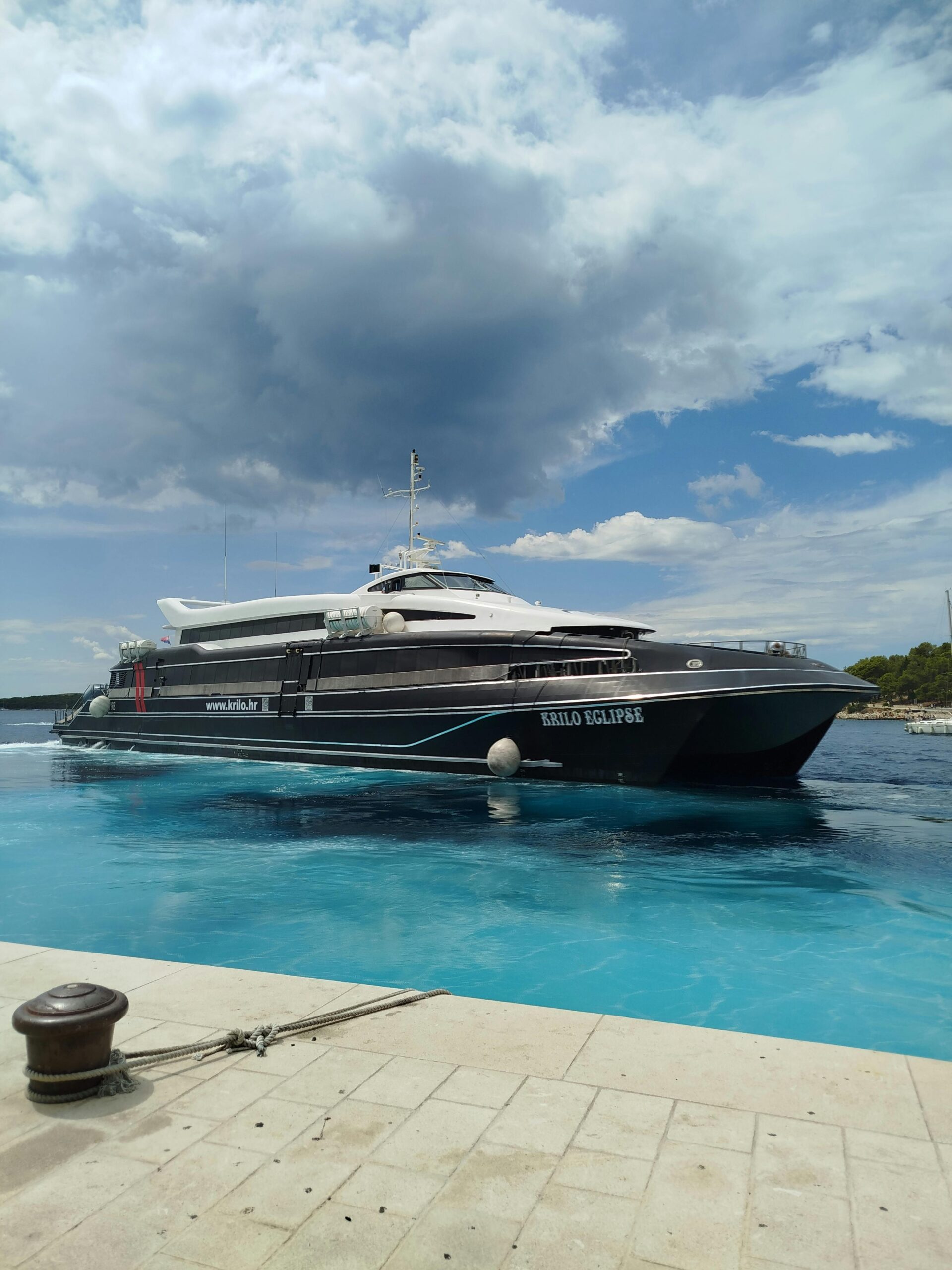 A luxurious yacht named Kollo Eclipse docked at a pier under a bright cloudy sky.